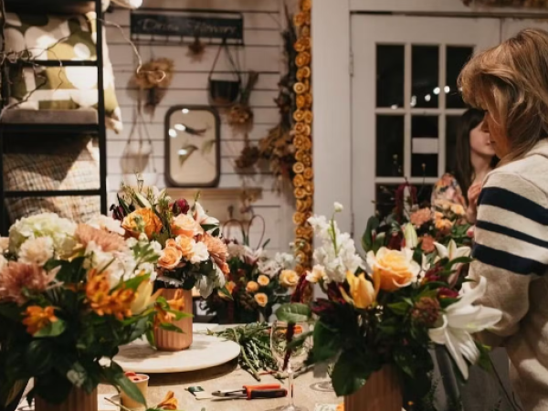 A cozy floral shop scene with two people arranging colorful flower bouquets on a table, surrounded by decor and tools.