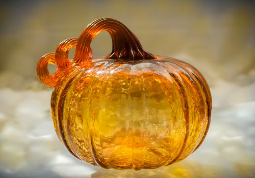 The image shows a glass sculpture of a pumpkin with a textured surface and curled stem, in an amber hue.
