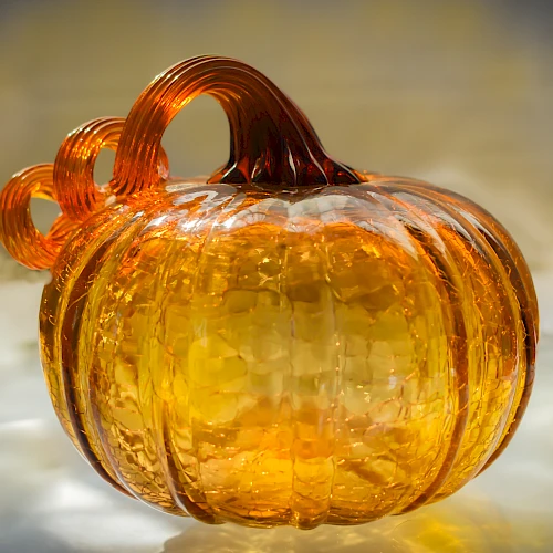 The image shows a glass sculpture of a pumpkin with a textured surface and curled stem, in an amber hue.