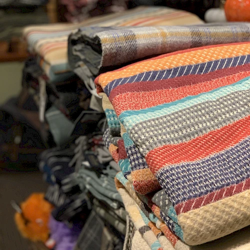 A stack of colorful, folded textiles or blankets with various patterns is displayed on a shelf.