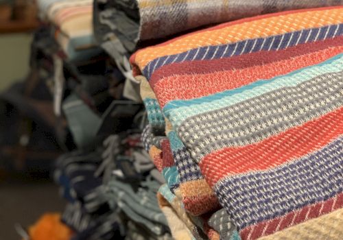 A stack of colorful woven blankets and textiles neatly folded on a display rack in a shop.