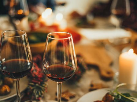 Two glasses of red wine on a candlelit dinner table with plates and dishes, creating a warm and cozy atmosphere.