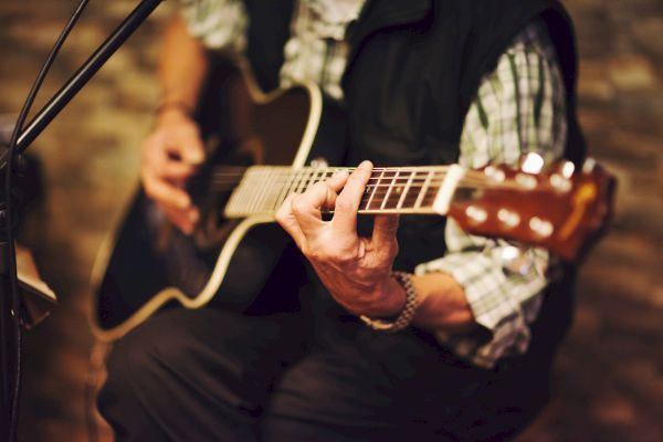 A person is playing an acoustic guitar, with focus on their hands and the instrument under soft lighting.