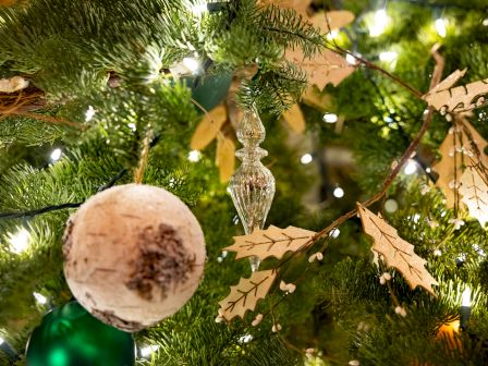 A Christmas tree decorated with a white bauble, glass ornament, lights, and golden leaves.